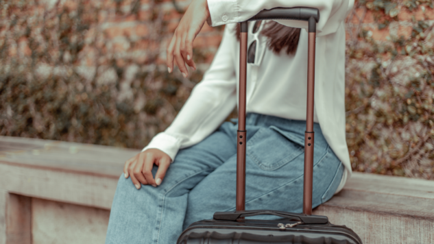 Woman sitting on a bench with her arm resting on an extended suitcase handle