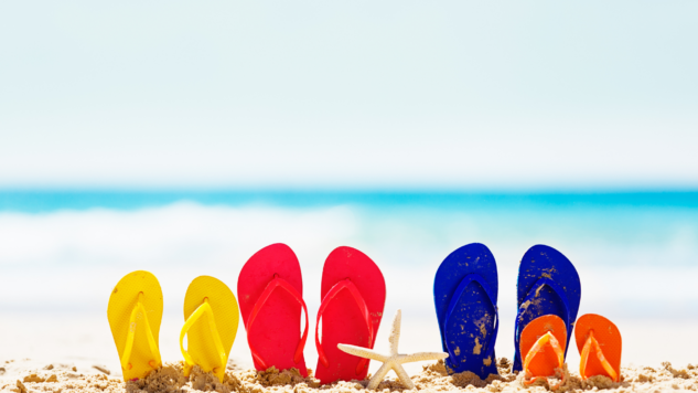 Yellow, Red, Blue and Orange sandals in foreground on a beach with a clear blue sky