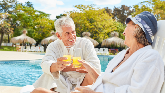 Mature couple relaxing on sun loungers by a pool, raising their glasses in a toast