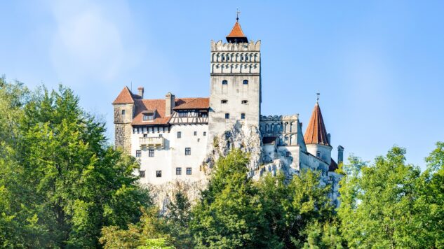 Daylight summer view to Bran Castle, with green trees in foreground. Bright, blue clear sky