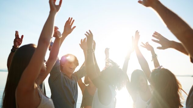 A group of people dancing together smiling with sunlight in background