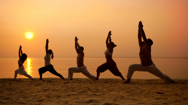 Image of 5 people performing a yoga pose on a beach at sunset