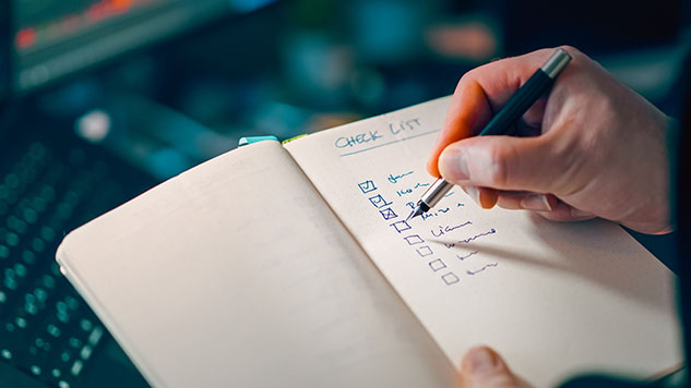 Hand ticking items off a handwritten checklist in a notebook.