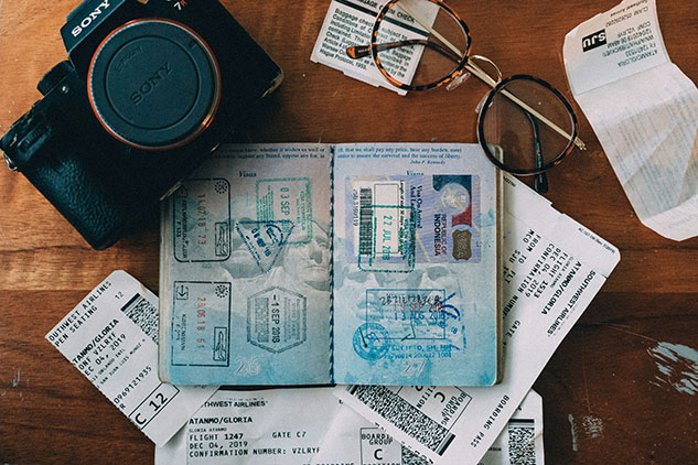 Open passport with travel stamps surrounded by boarding passes, glasses and a camera on a wooden table.