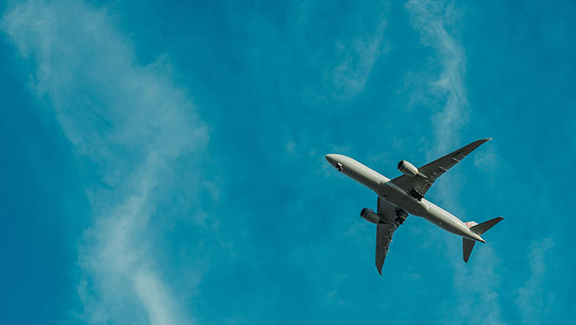 A plane flying overhead against a bright blue sky with scattered clouds.